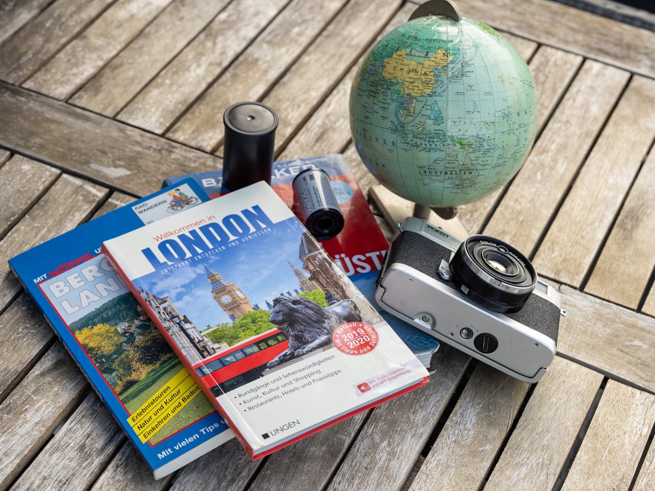 creative-01 A vintage travel setup with guidebooks, a globe, and a film camera on a wooden table.