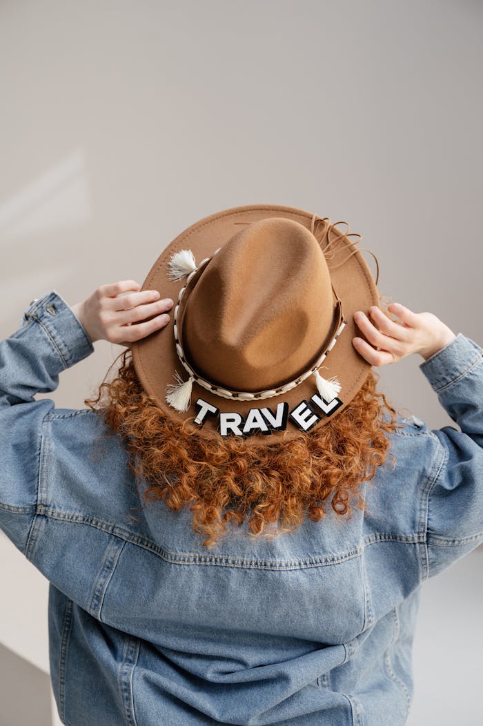 digital-01 Red-haired woman wearing a travel-themed fedora and denim jacket, viewed from behind.